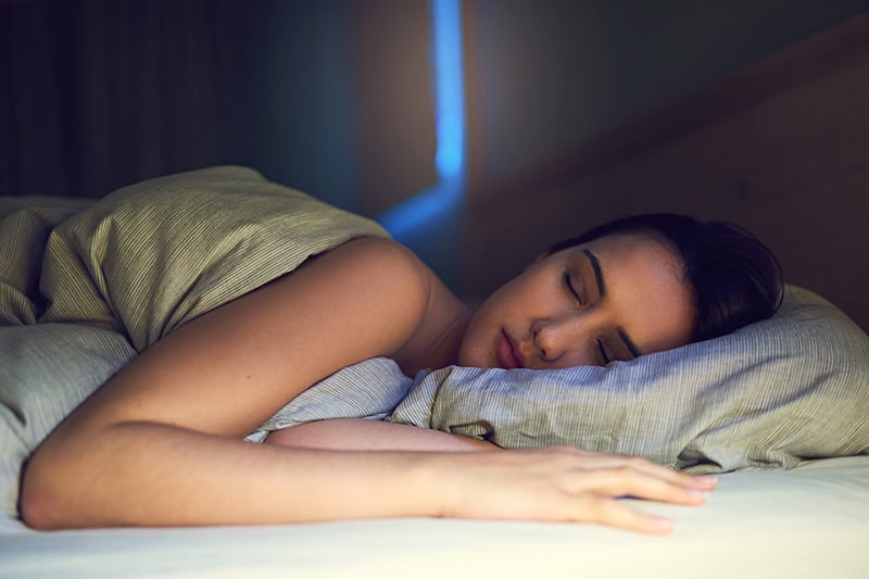 3 Health Benefits of Using Your AC While Sleeping. Photo of a young woman sleeping.